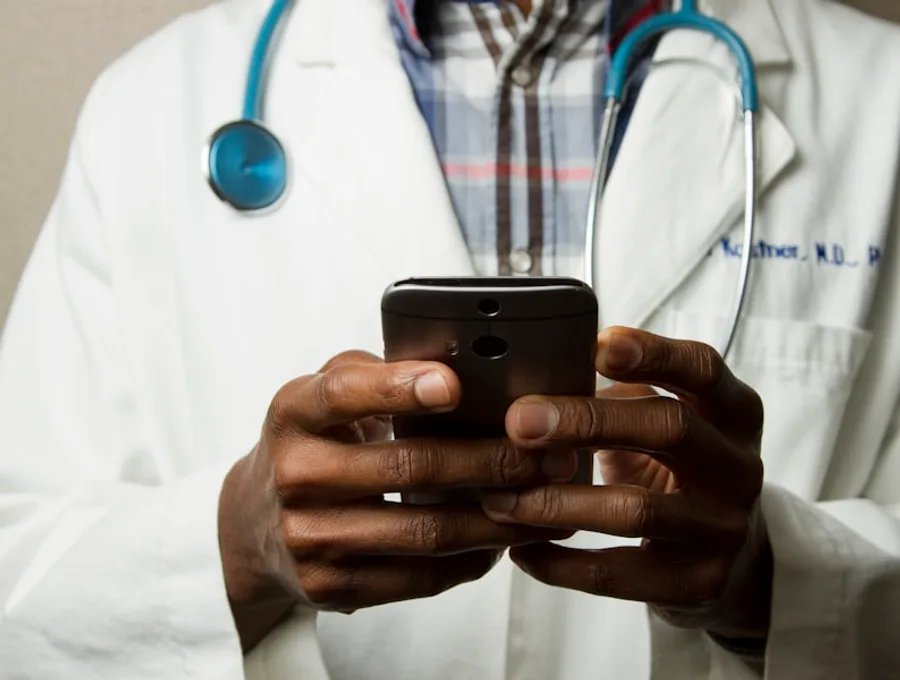 A clinician in a white coat and stethoscope using a phone