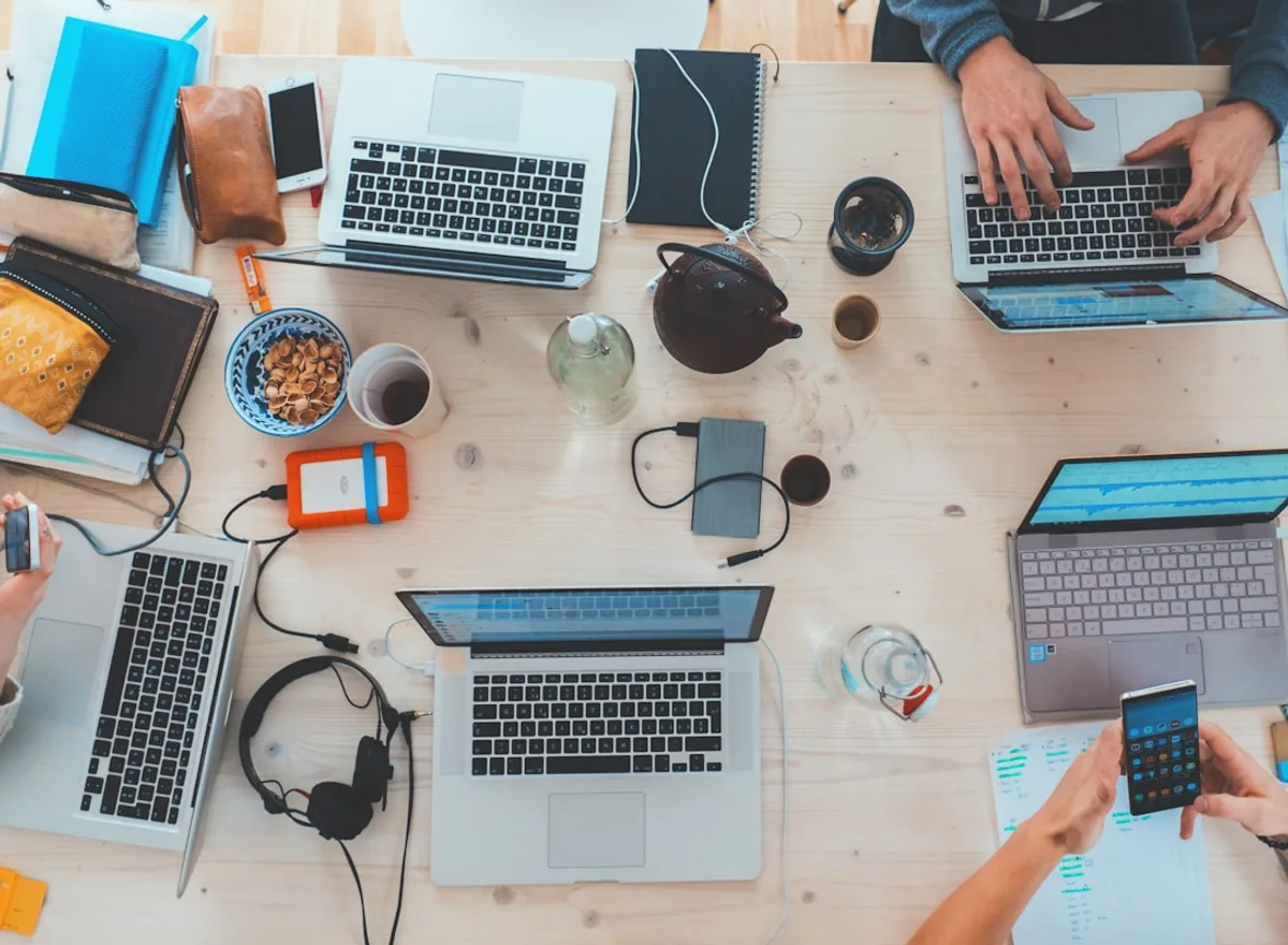 A worktable covered with laptops, phones and headphones